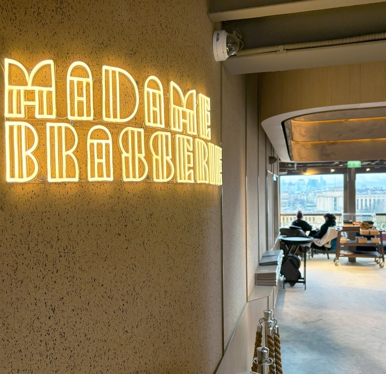 The interior of 'Madame Brasserie' lit with a warm glow, featuring a neon sign, poised to welcome guests to a premium dining and photography experience