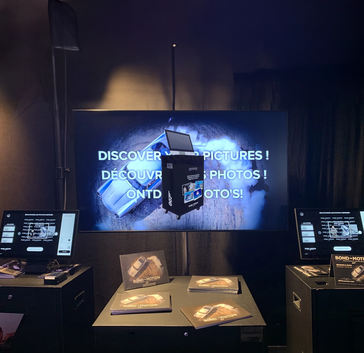 Interactive photo stations at the 'Bond in Motion' exhibition displaying the 'DISCOVER YOUR PICTURES!' screen, inviting visitors to print their photos