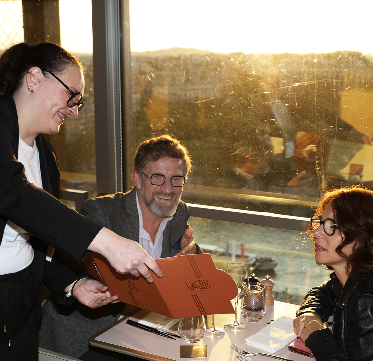 A server presents a couple with a printout of their photos during a fine dining experience, adding a personal touch to the meal.