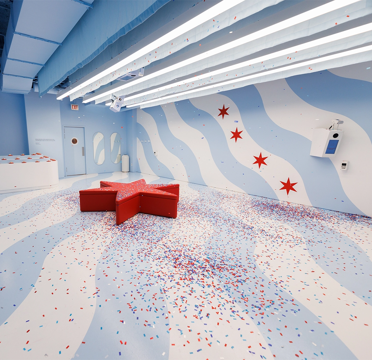 The floor is littered with colorful confetti in a room designed with wavy blue patterns and star decorations, offering a playful photo op at the Color Factory