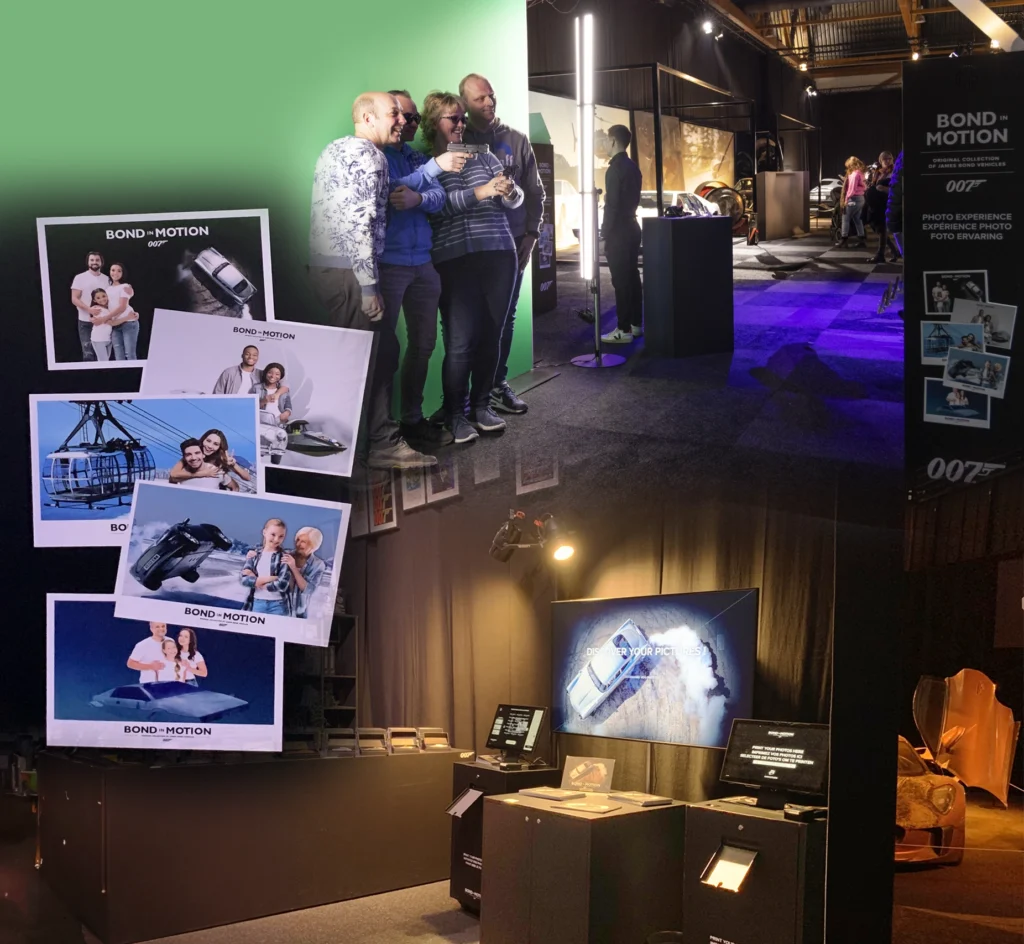 Hosté pózují při fotografování s rekvizitami s bondovskou tématikou na výstavě "Bond in Motion" s ukázkami fotografií vystavenými na stěně.