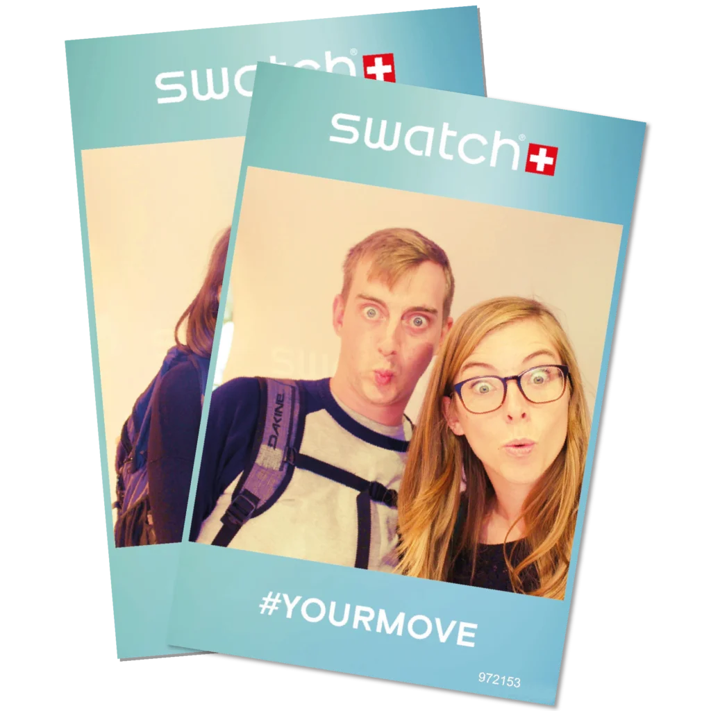 Gewinnspiel Swatch. Zwei verspielte Freunde, die ihre mit Swatch gebrandeten Fotoausdrucke mit komischen Gesichtsausdrücken hochhalten und damit ihre persönlichen Momente in Amsterdam hervorheben